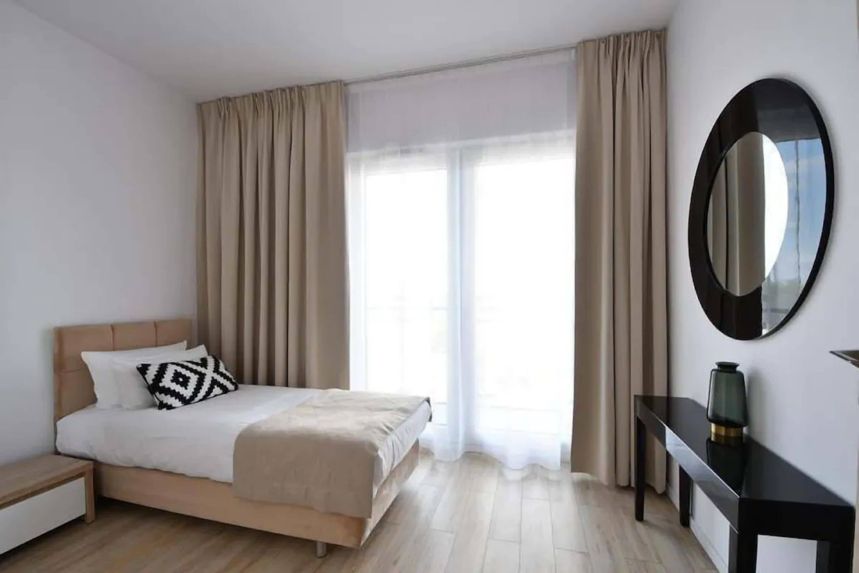 Et moderne hotelværelse med en seng, et natbord, et spejl og udsigt til det fri gennem store vinduer.