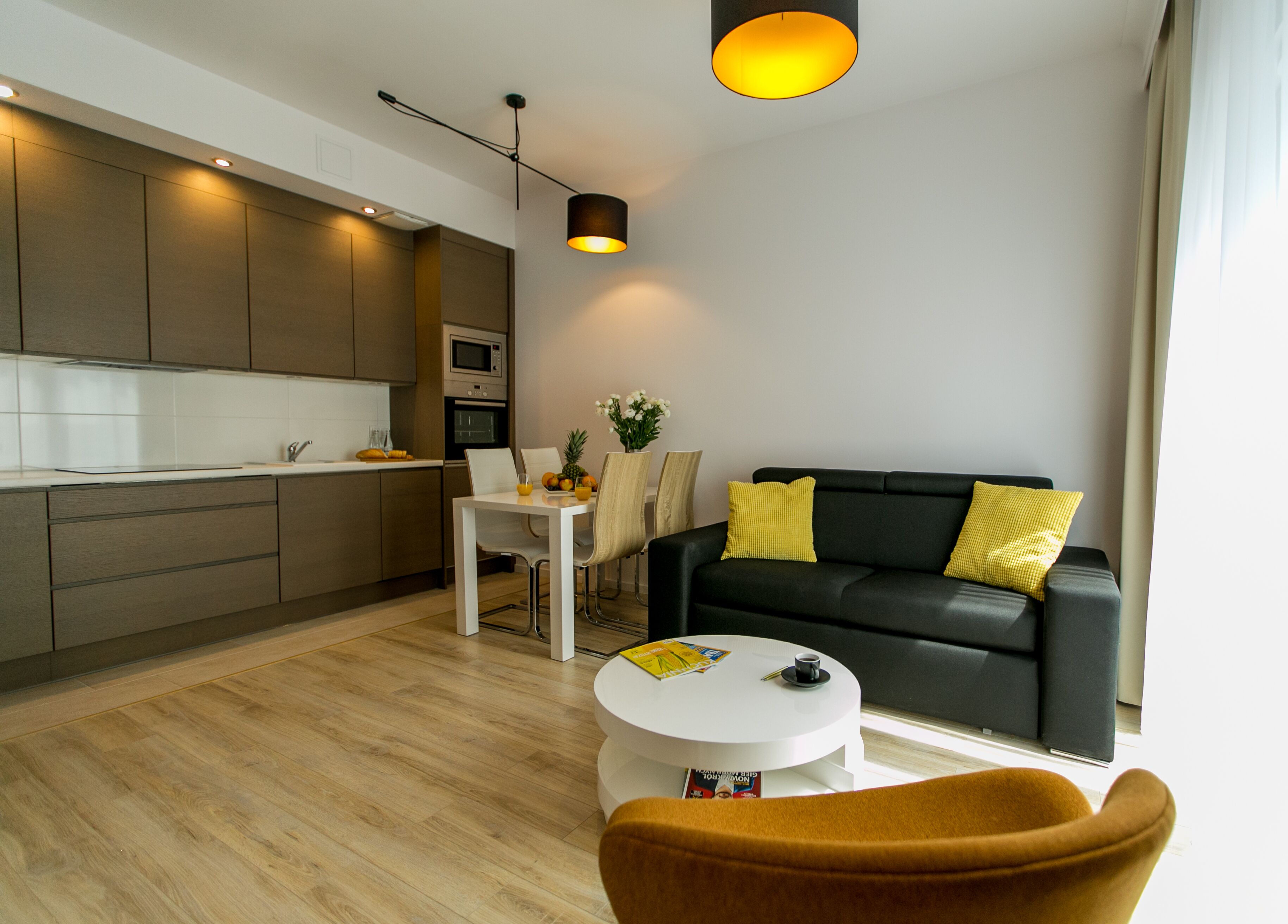 A modern living room with a black sofa, yellow pillows, a white coffee table, and a brown armchair.