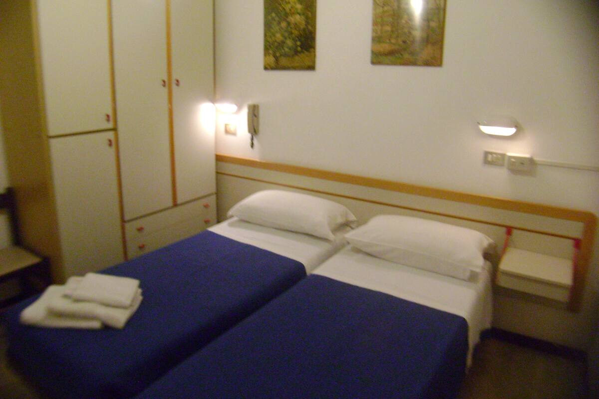 A hotel room with two single beds, a wardrobe, and two wall-mounted light fixtures.
