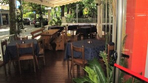 An outdoor dining area with tables and chairs, surrounded by greenery and a covered walkway.