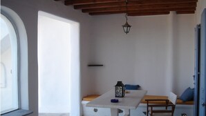 Een kamer met een witte tafel, een houten bank, een hangende lantaarn en een deur.