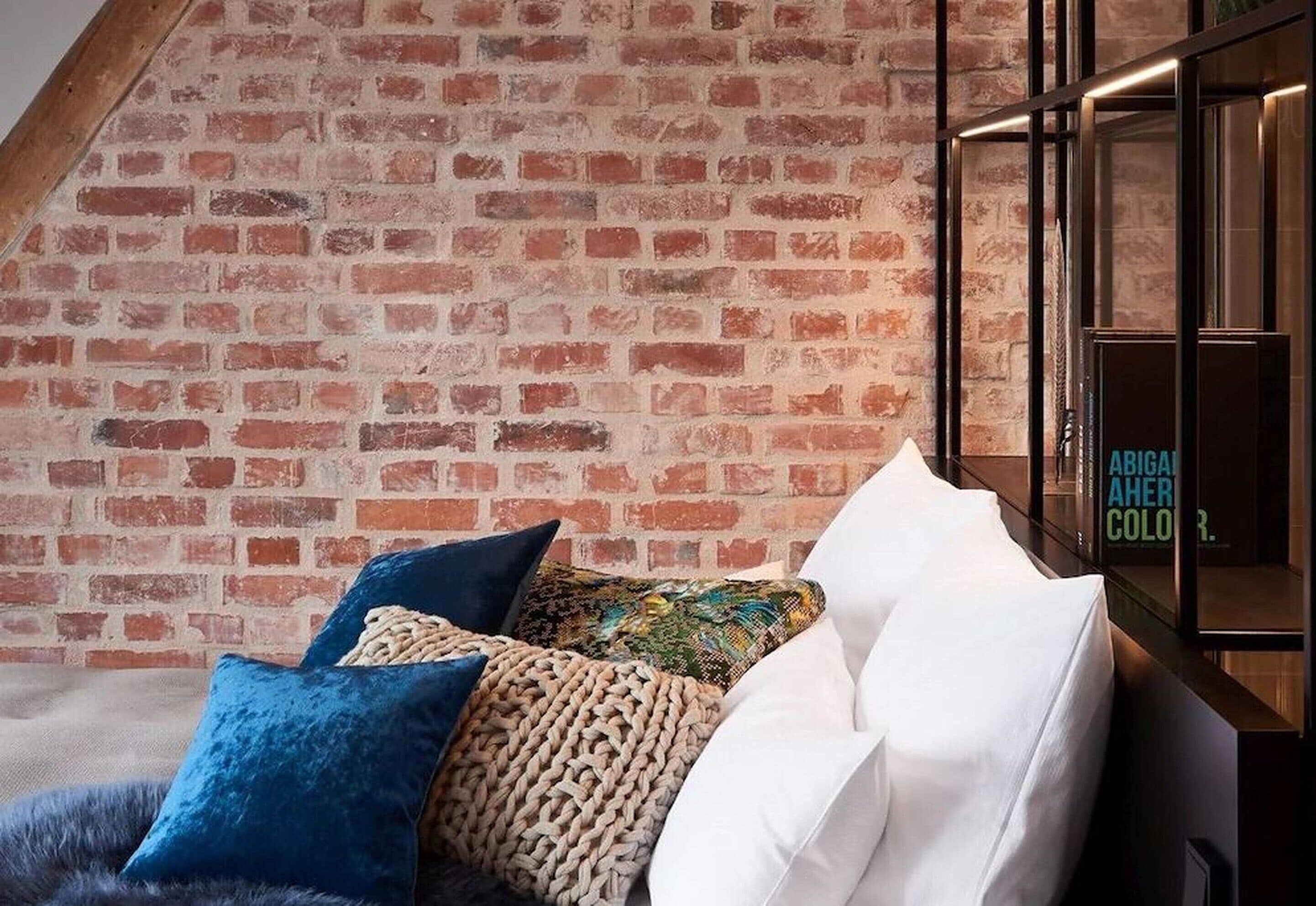 Ein Zimmer mit Backsteinwand, einer Couch mit verschiedenen Kissen und einer Kommode mit einem Schild.