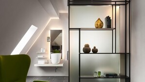 A modern interior with a green armchair, a white console table, and a glass shelving unit with decorative items. - Aparthotel Mittermeiers Alter Ego (Rothenburg ob der Tauber)