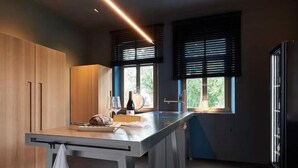 A modern kitchen with wooden cabinets, a countertop, and a window with blinds. - Aparthotel Mittermeiers Alter Ego (Rothenburg ob der Tauber)