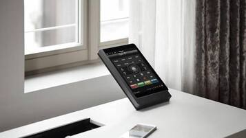 A modern room with a desk, a smartphone, and a digital control panel.