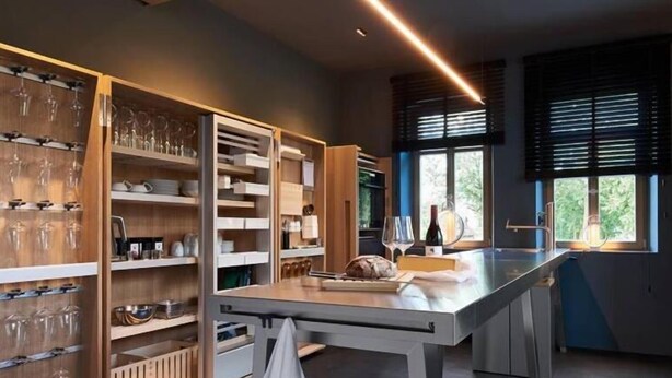 A modern kitchen with built-in shelves for glassware, a central island, and large windows with blinds. - Aparthotel Mittermeiers Alter Ego (Rothenburg ob der Tauber)
