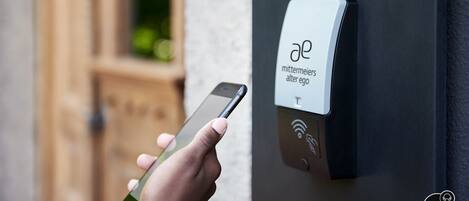 A hand holding a smartphone in front of a smart lock with a label reading "mittemeiers alter ego".