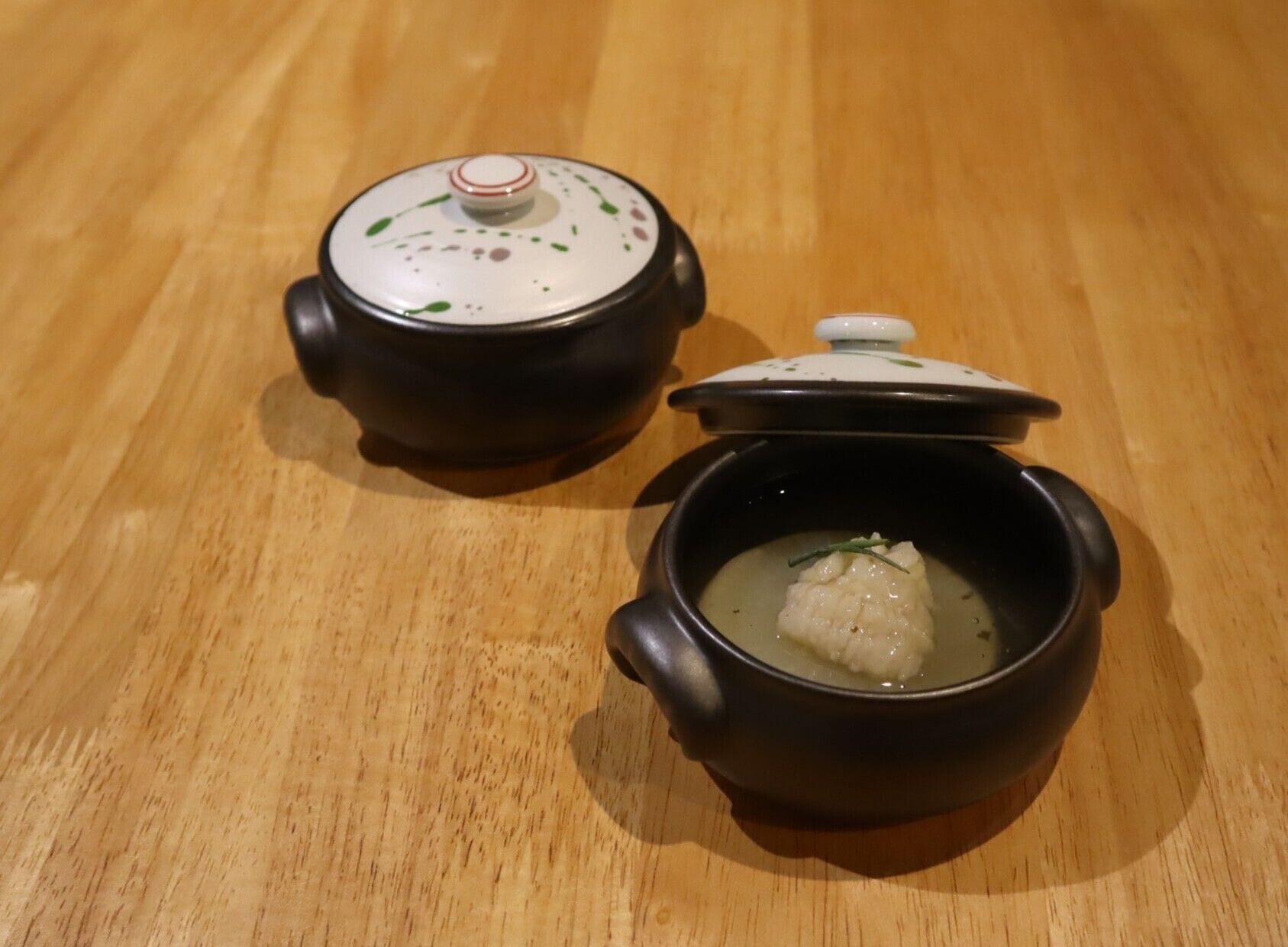 Two black ceramic pots with lids on a wooden surface.