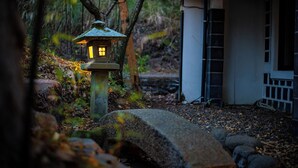 A traditional Japanese lantern in a forested area with a building in the background. - Beppu Tabiyado Sainokou (Beppu)