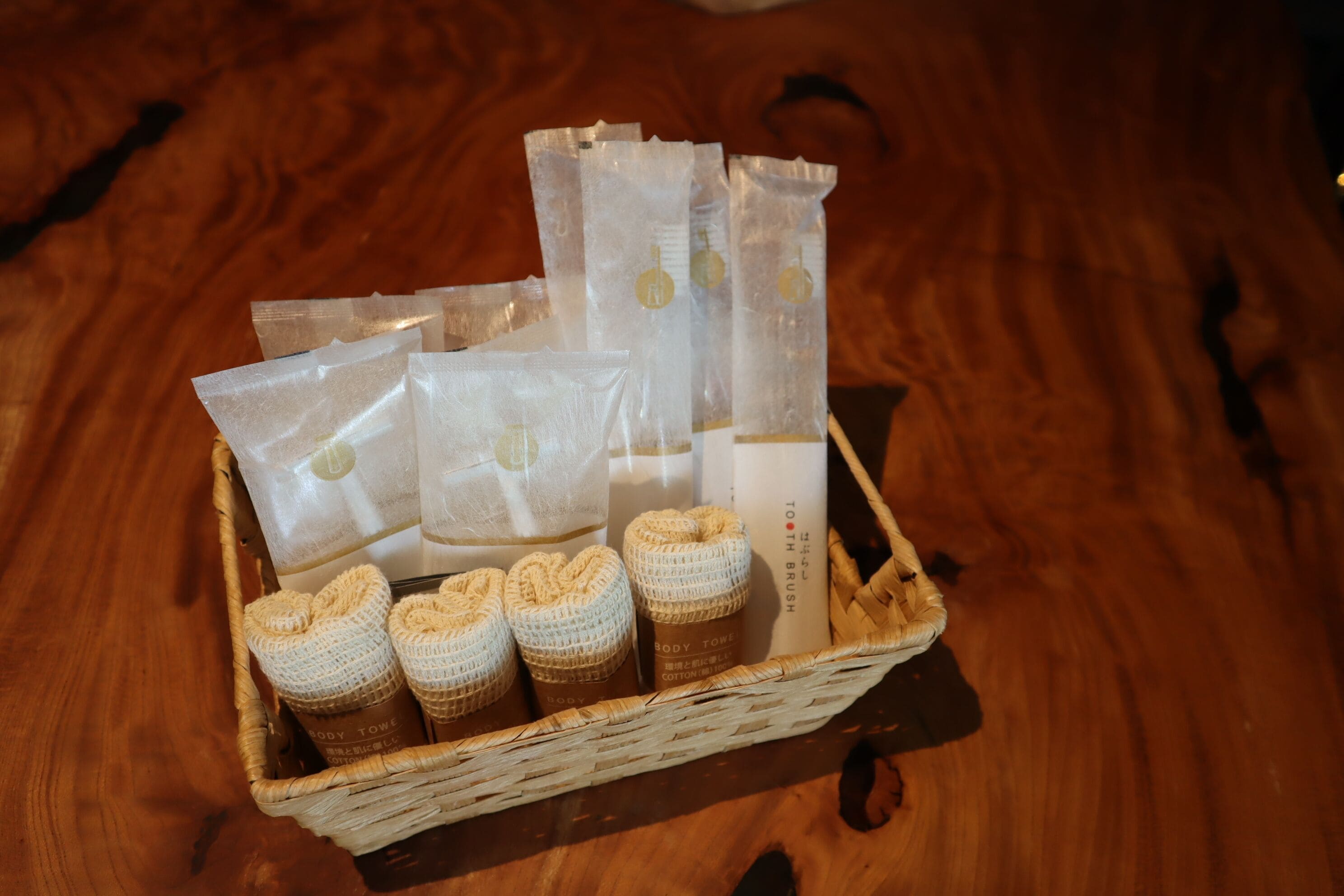 A wicker basket containing various toiletries and a body towel on a wooden surface.