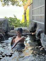 A person in a natural setting with a wooden structure and rocks.
