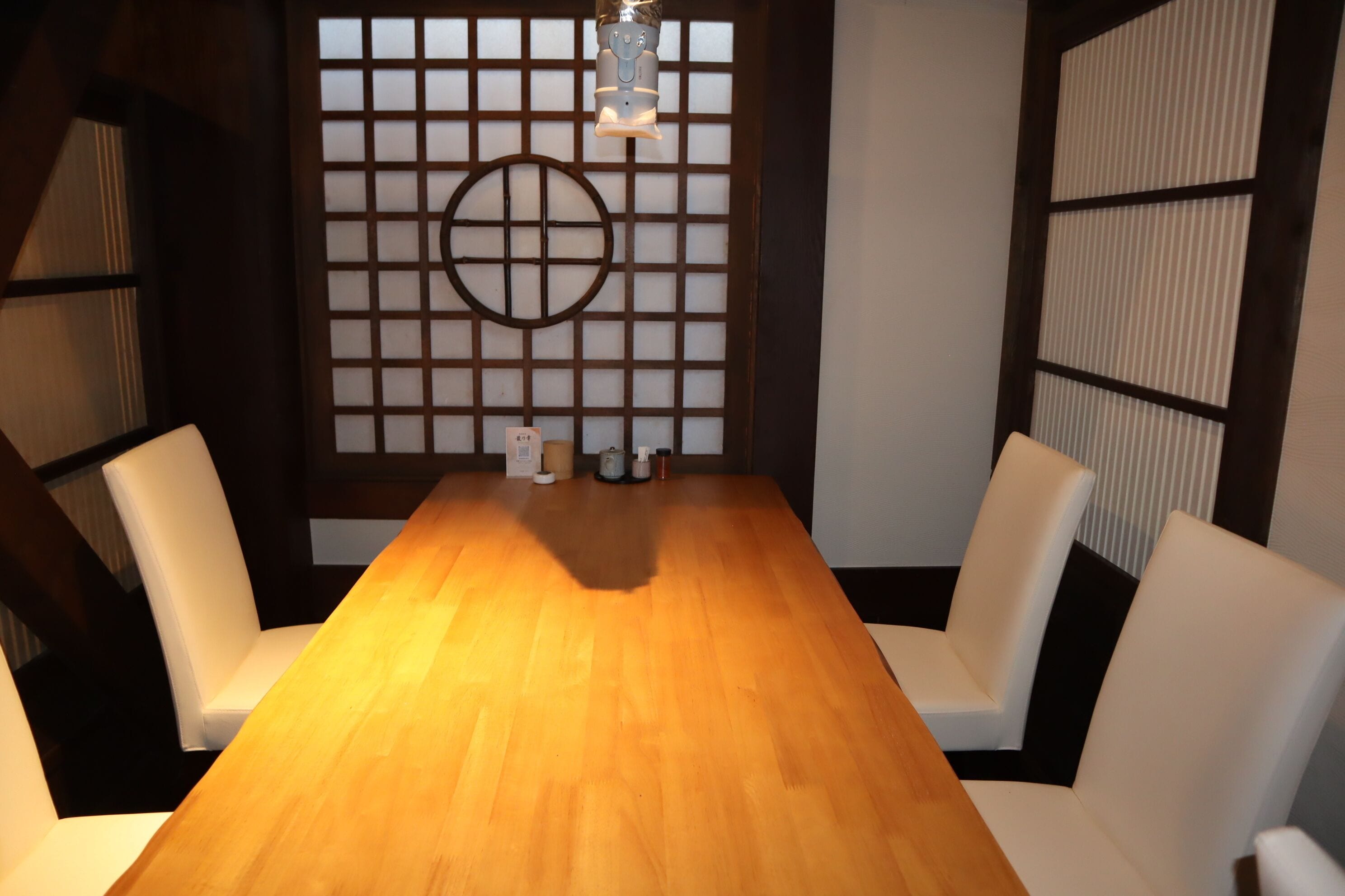 A conference room with a wooden table, white chairs, a decorative wall with a grid pattern, and a hanging light fixture.