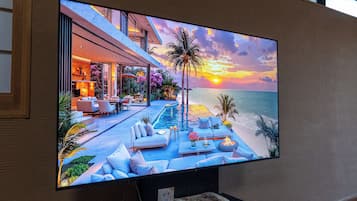 A flat-screen TV displaying a sunset view over a pool with lounge chairs and a dining area.