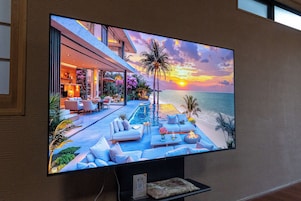 A flat-screen TV displaying a sunset view over a pool with lounge chairs and a dining area.