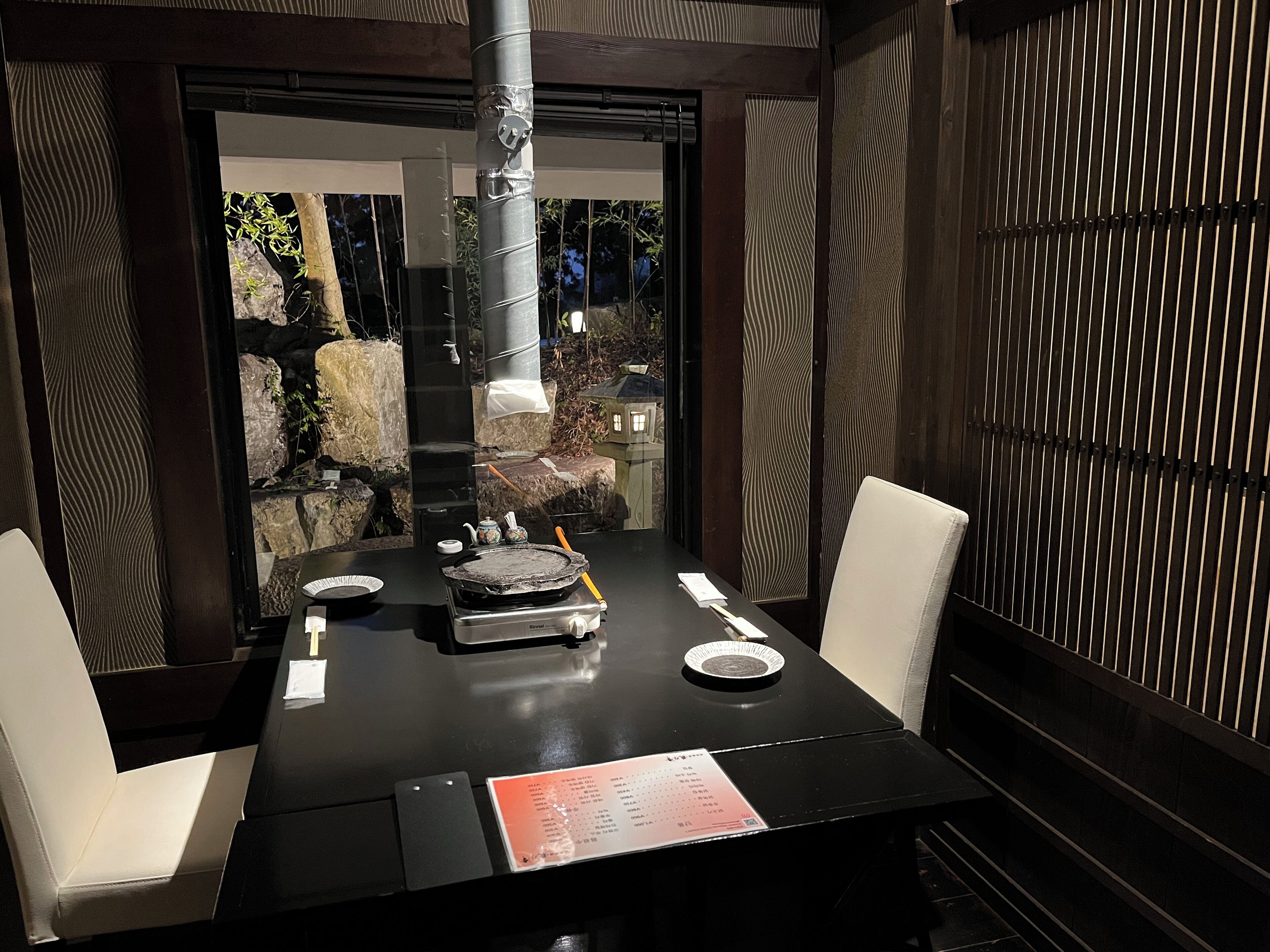 A dining area with a black table, white chairs, a menu, and a teapot.