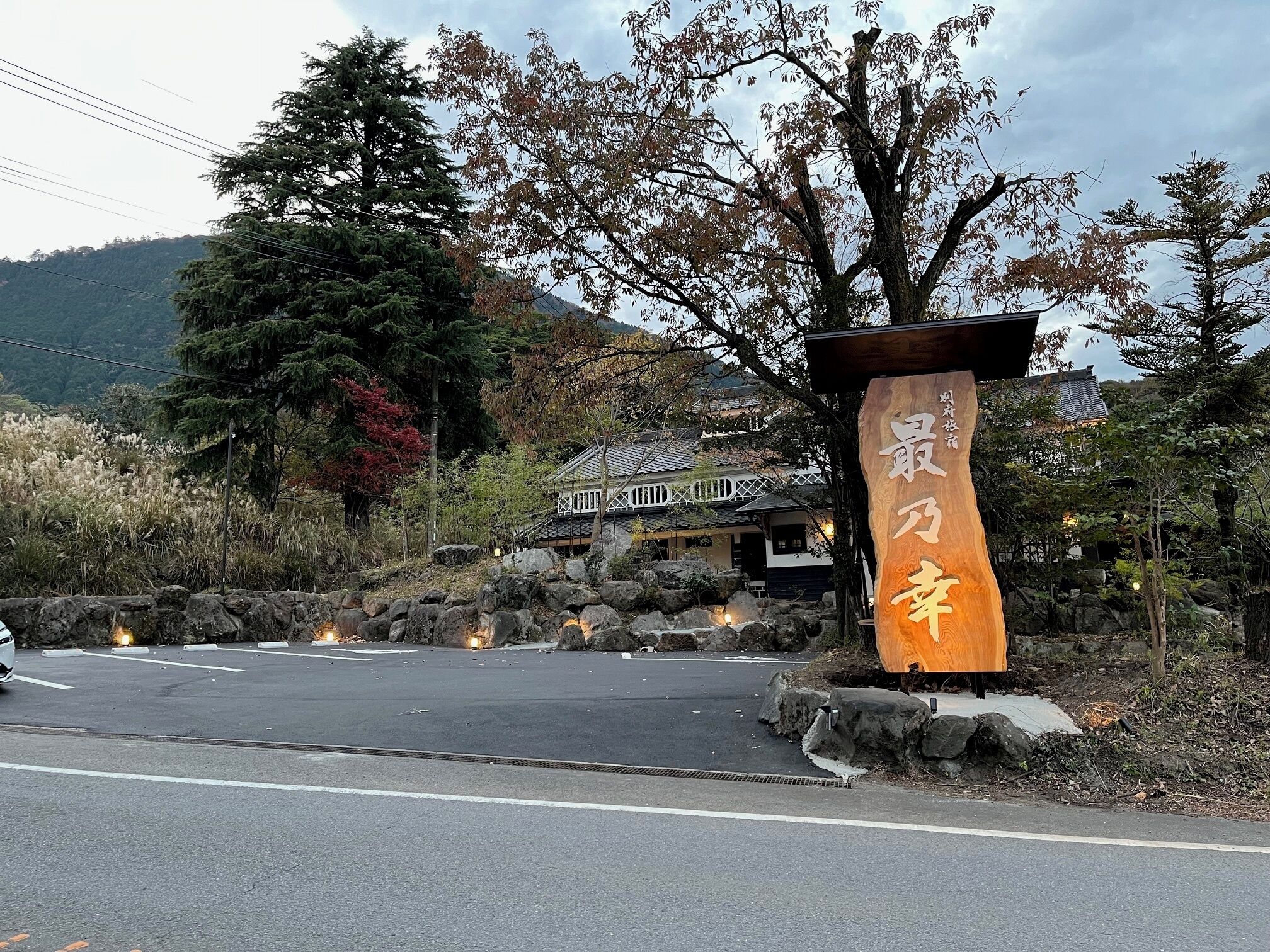 A traditional Japanese building with a stone pathway leading to it, surrounded by trees and a mountainous backdrop.