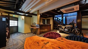 A hotel lobby with a reception desk, a motorcycle, and a wooden table. - Beppu Tabiyado Sainokou (Beppu)