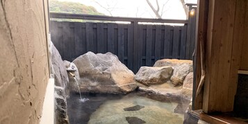 Un área de aguas termales con grandes rocas y una valla de madera al fondo.