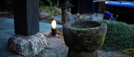Una estructura de piedra cubierta de musgo, un banco de piedra y una pequeña vela encendida en el suelo.