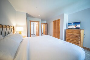 A hotel room with a large bed, a wooden dresser, a television, and a lamp. - Expedition Station 8614 (Keystone)
