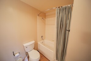 A bathroom with a toilet, a bathtub, and a shower curtain. - Expedition Station 8614 (Keystone)