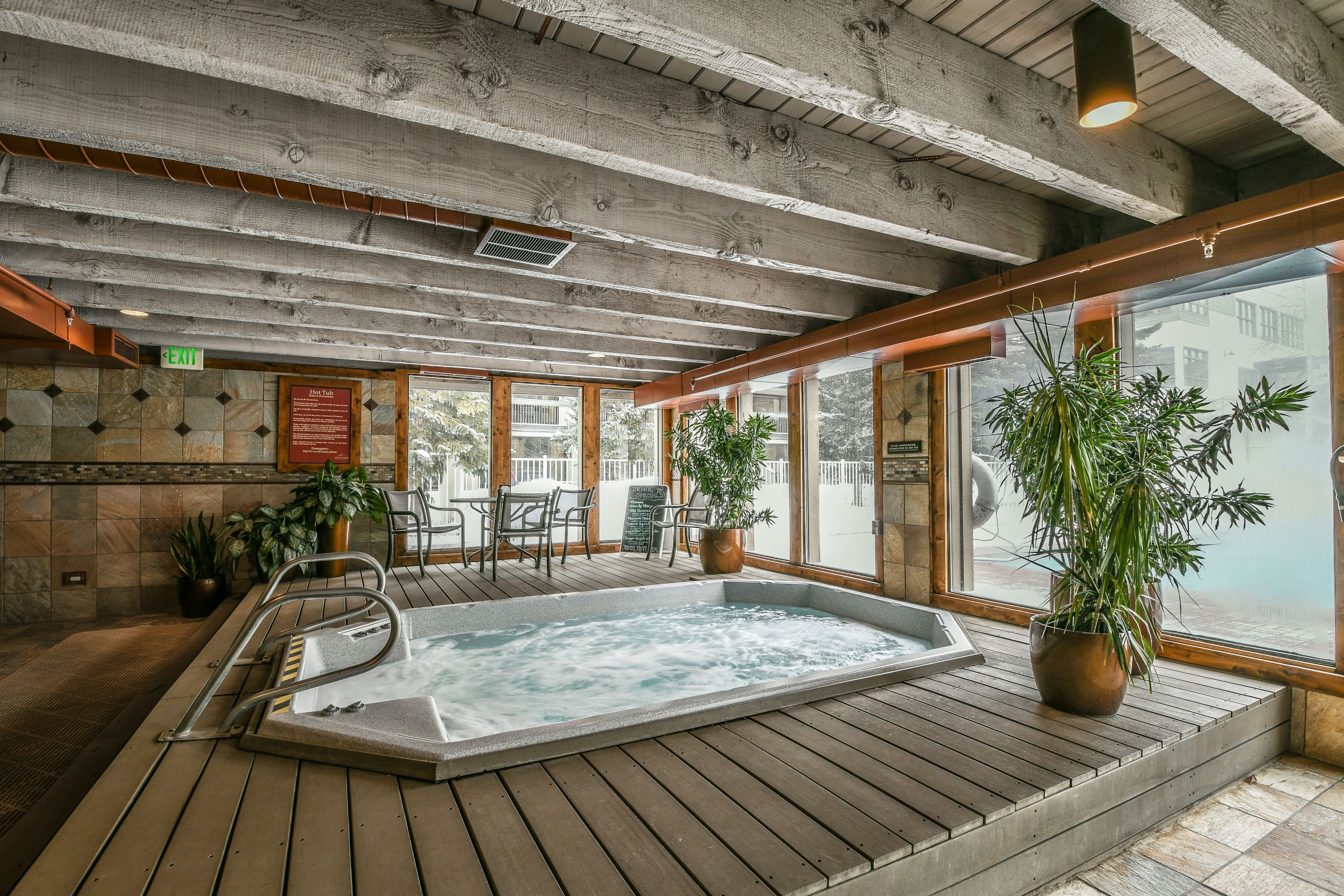 Terraza de madera con hidromasaje, plantas en macetas y vista al exterior.