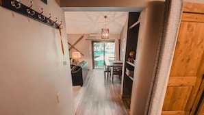 A hallway with a wooden floor, a coat rack, a cross-shaped light fixture, and a view of an outdoor area through a glass door. - Flying Dutchman 1174 (Keystone)