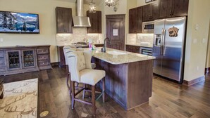 A modern kitchen with dark wood cabinets, a stainless steel refrigerator, and a large island with bar stools. - River Run Townhomes 96 (Keystone)