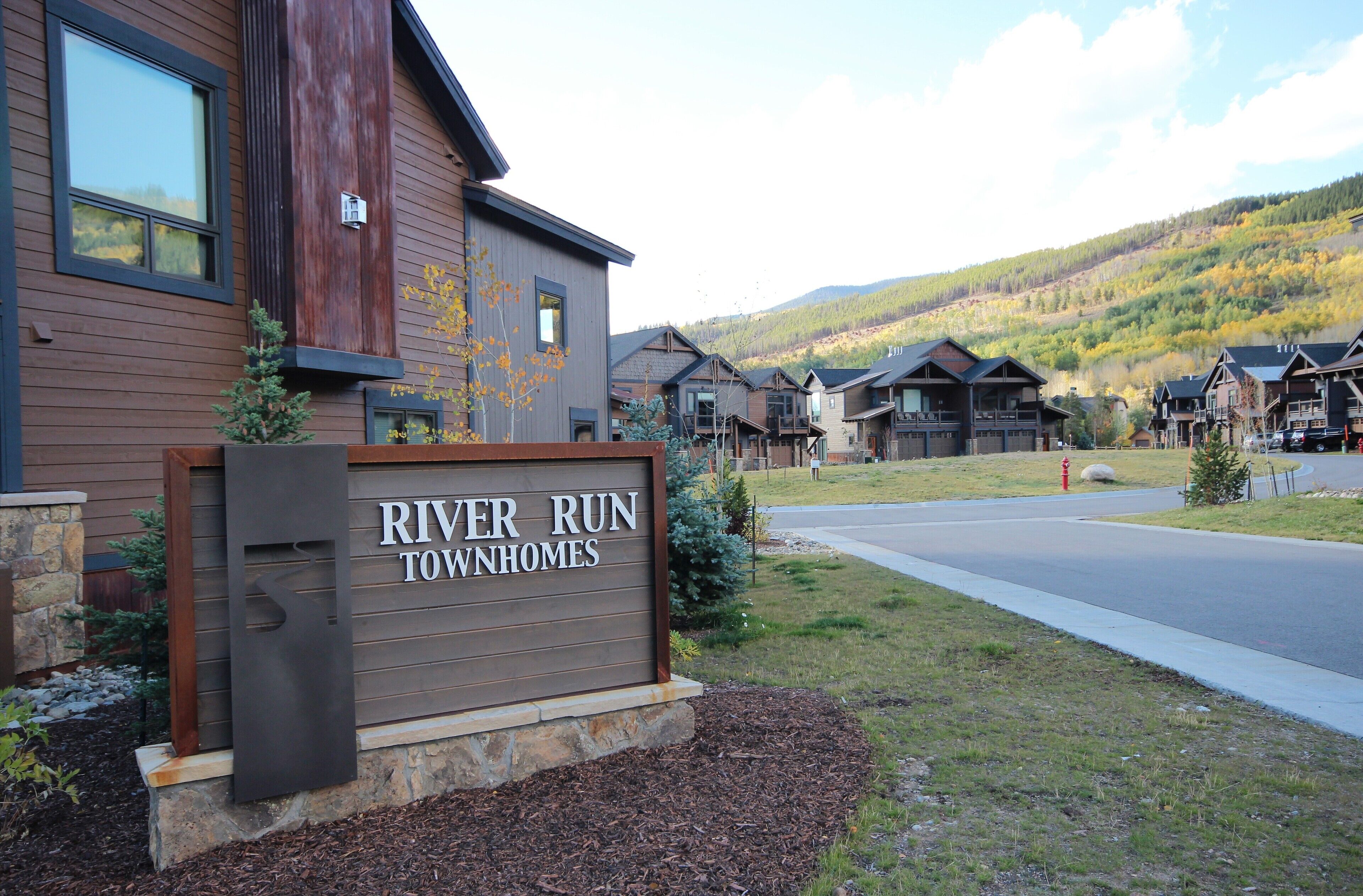 Une enseigne indiquant l’emplacement du complexe résidentiel River Run Townhomes, avec en arrière-plan une vue sur un quartier résidentiel et des montagnes.