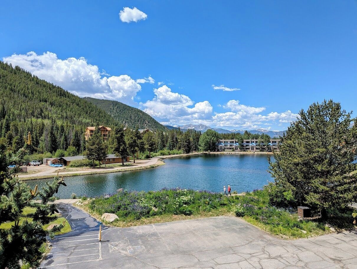 Un lago rodeado de colinas boscosas, un área de estacionamiento y edificios con vistas al lago.