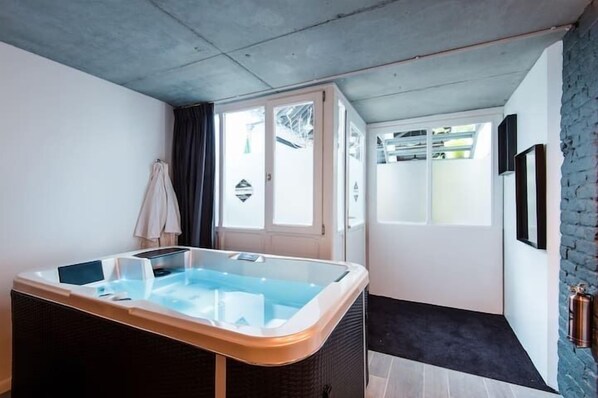 A modern room with a glass-enclosed hot tub, a door leading to a balcony, and a brick wall. - Le Comptoir industriel (Lille)
