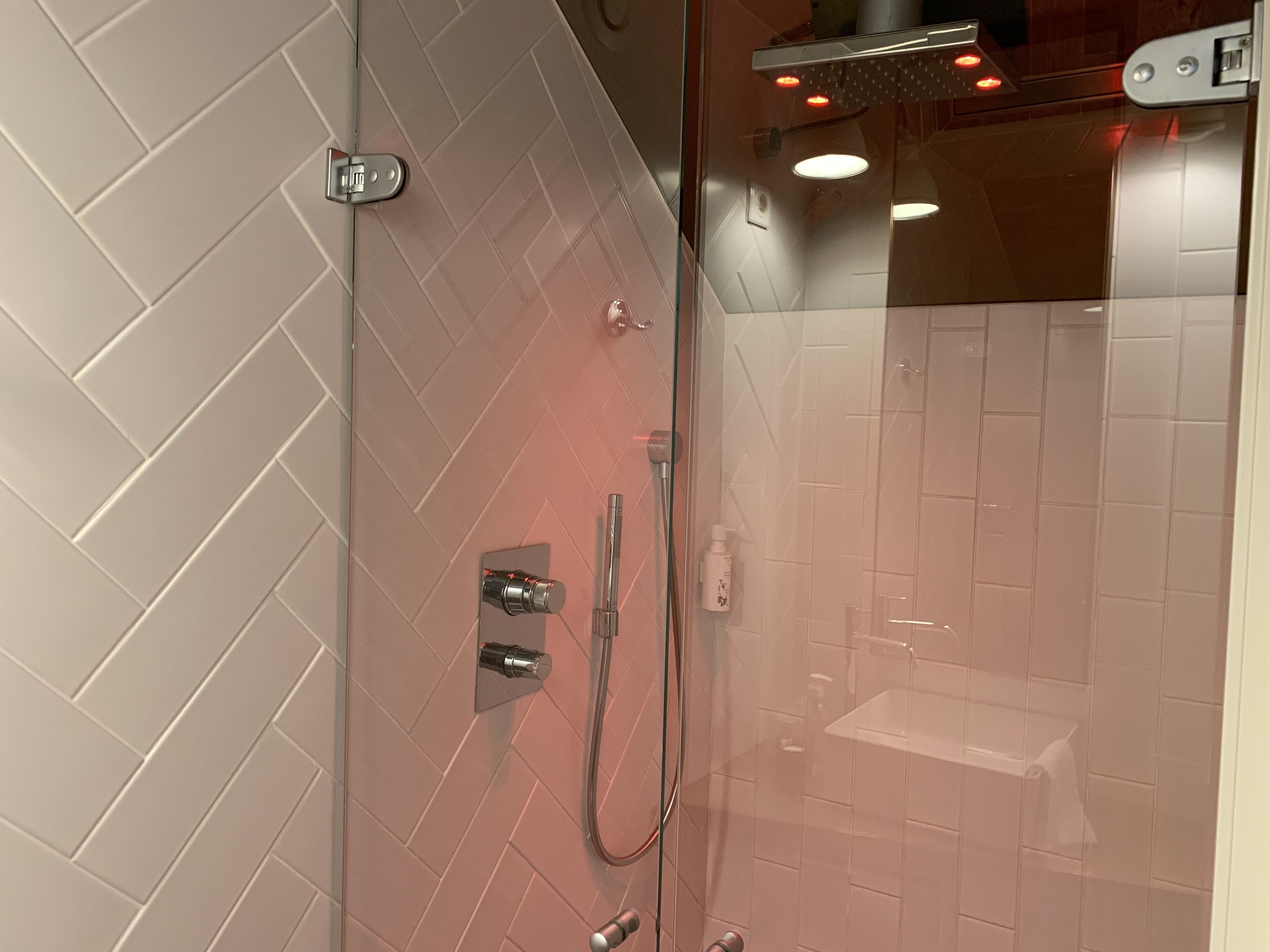 A modern bathroom with a glass-enclosed shower, white herringbone-patterned tiles, and a visible towel rack.