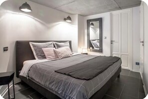 A modern bedroom with a large bed, a bedside table, a mirror, and a wardrobe. - Le Comptoir industriel (Lille)
