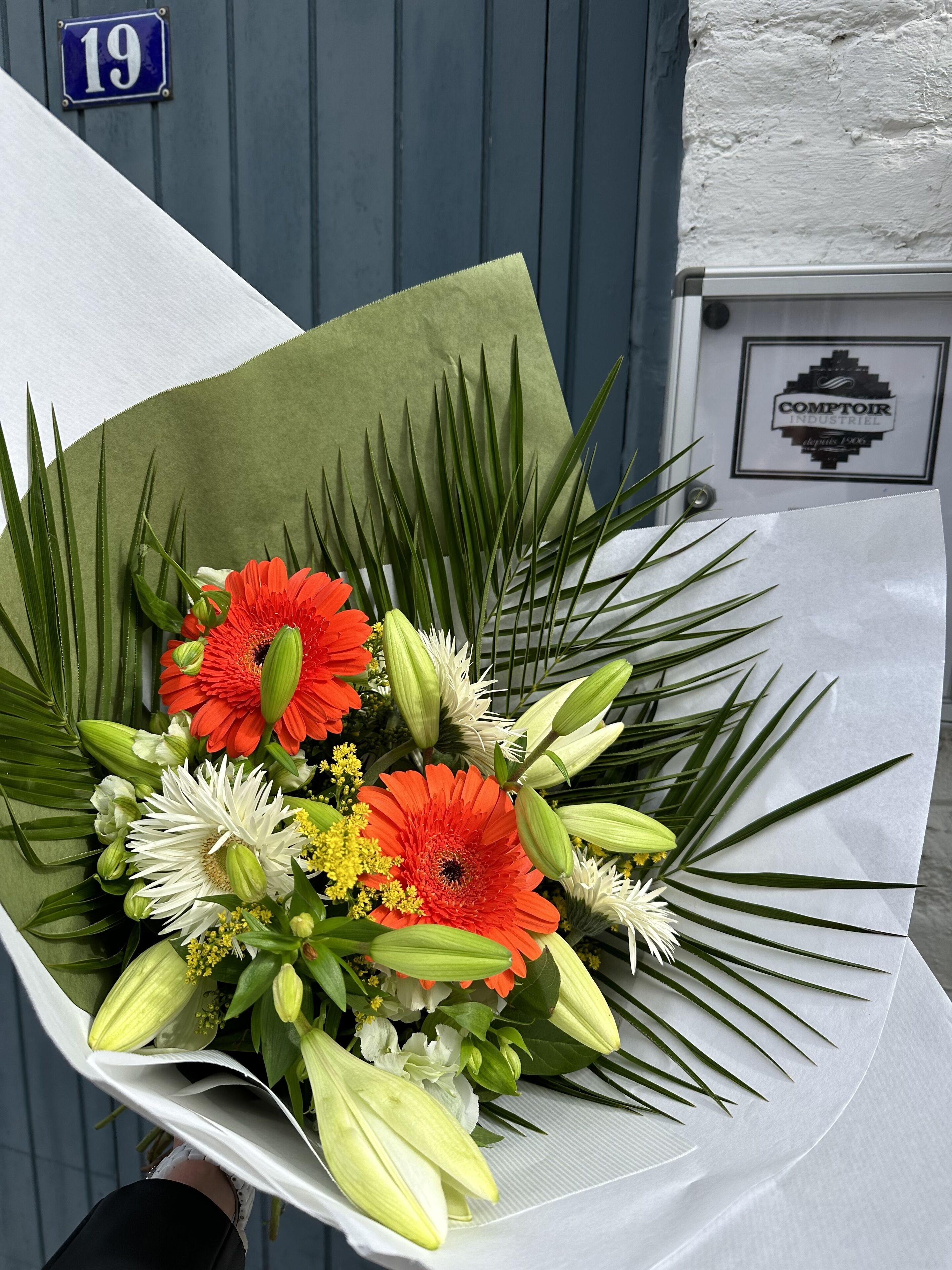 A bouquet of flowers with green leaves and a blue sign with the number 19 in the background.
