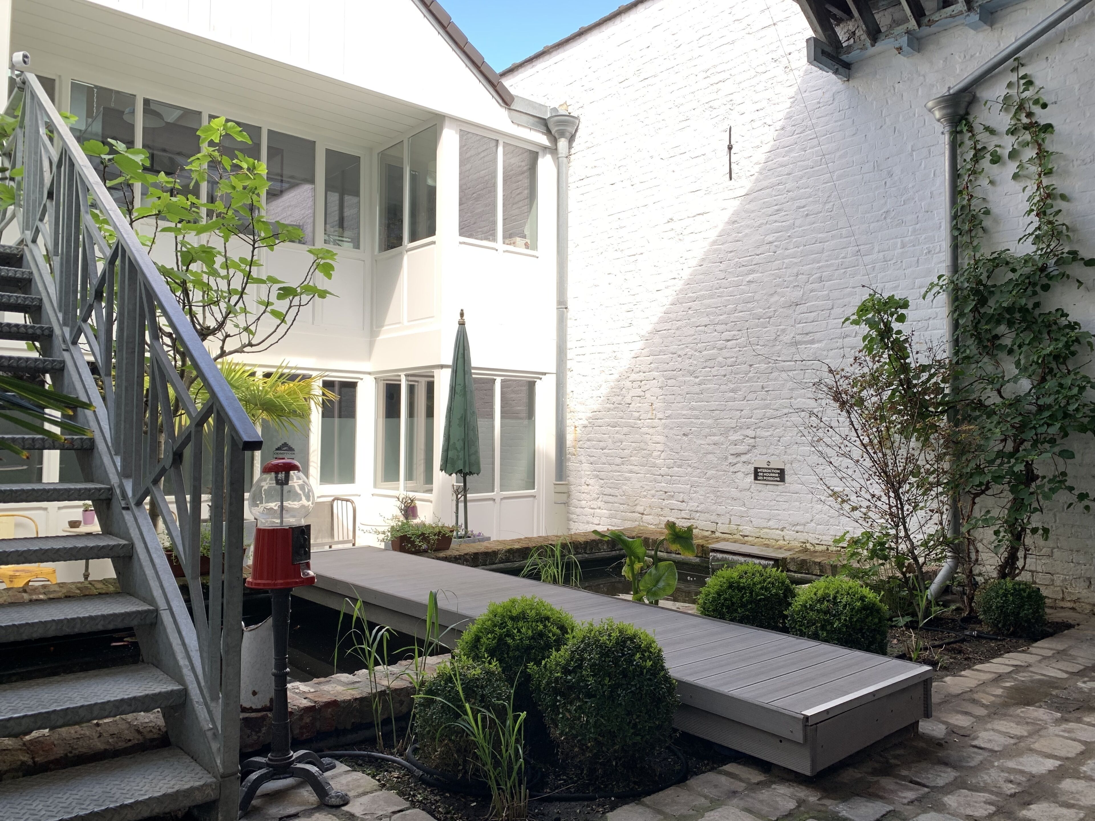 A white building with a staircase, a small deck, and a garden area with potted plants and a water feature.