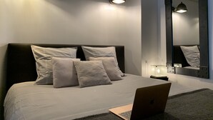Un dormitorio moderno con una cama grande, un ordenador portátil sobre la mesita de noche y un espejo grande en la pared.