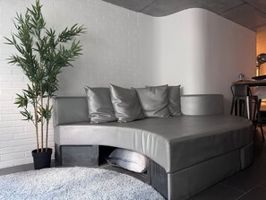A modern living room with a sofa, a potted plant, and a small table with a chair. - Le Comptoir industriel (Lille)