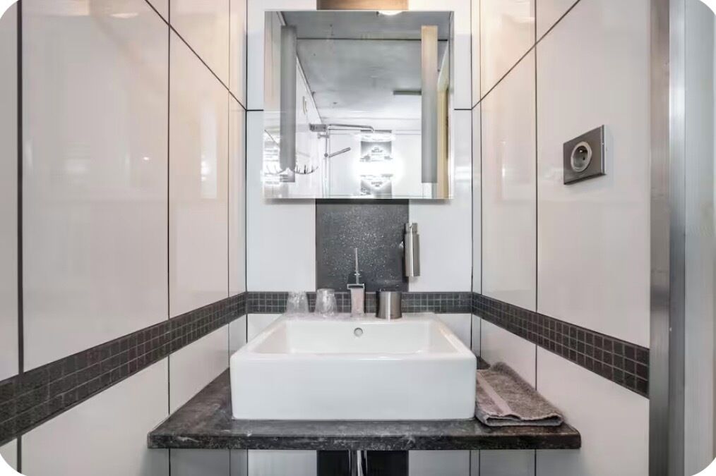 Un baño con un lavabo blanco, un espejo encima y una toalla sobre la encimera.
