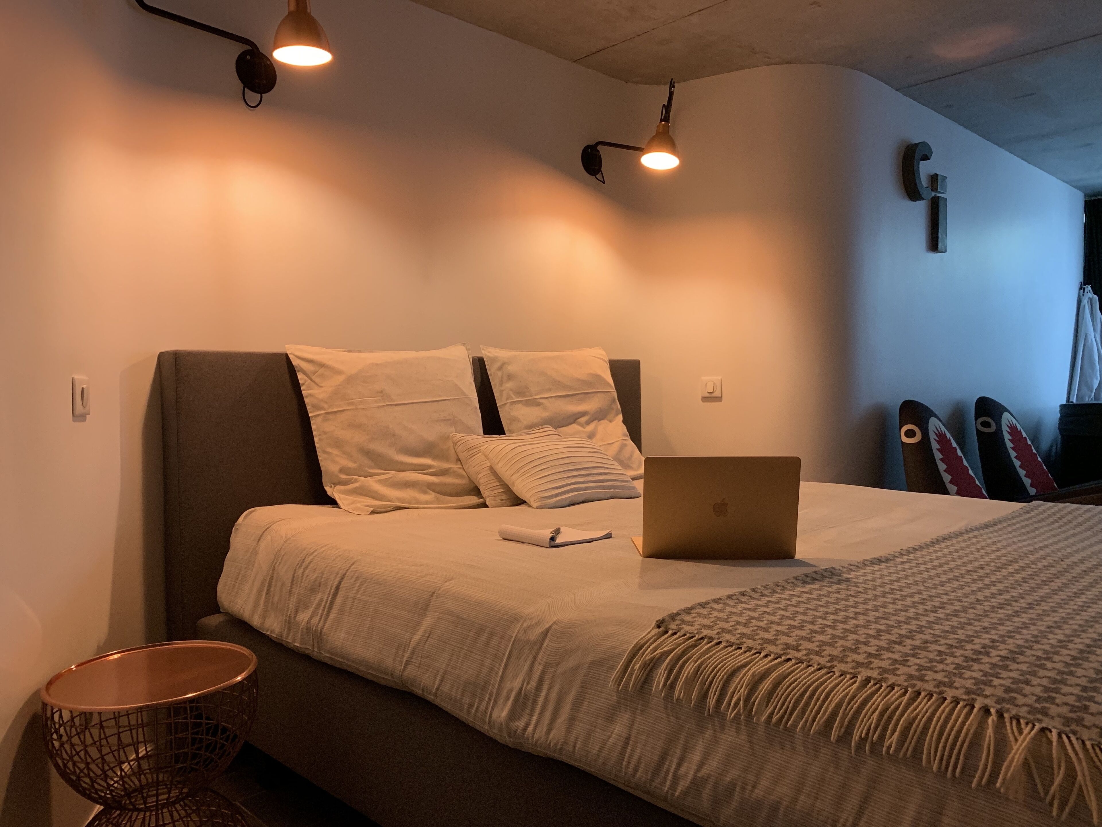 A bedroom with a bed, a laptop, a pair of skis, and a wall-mounted light fixture.