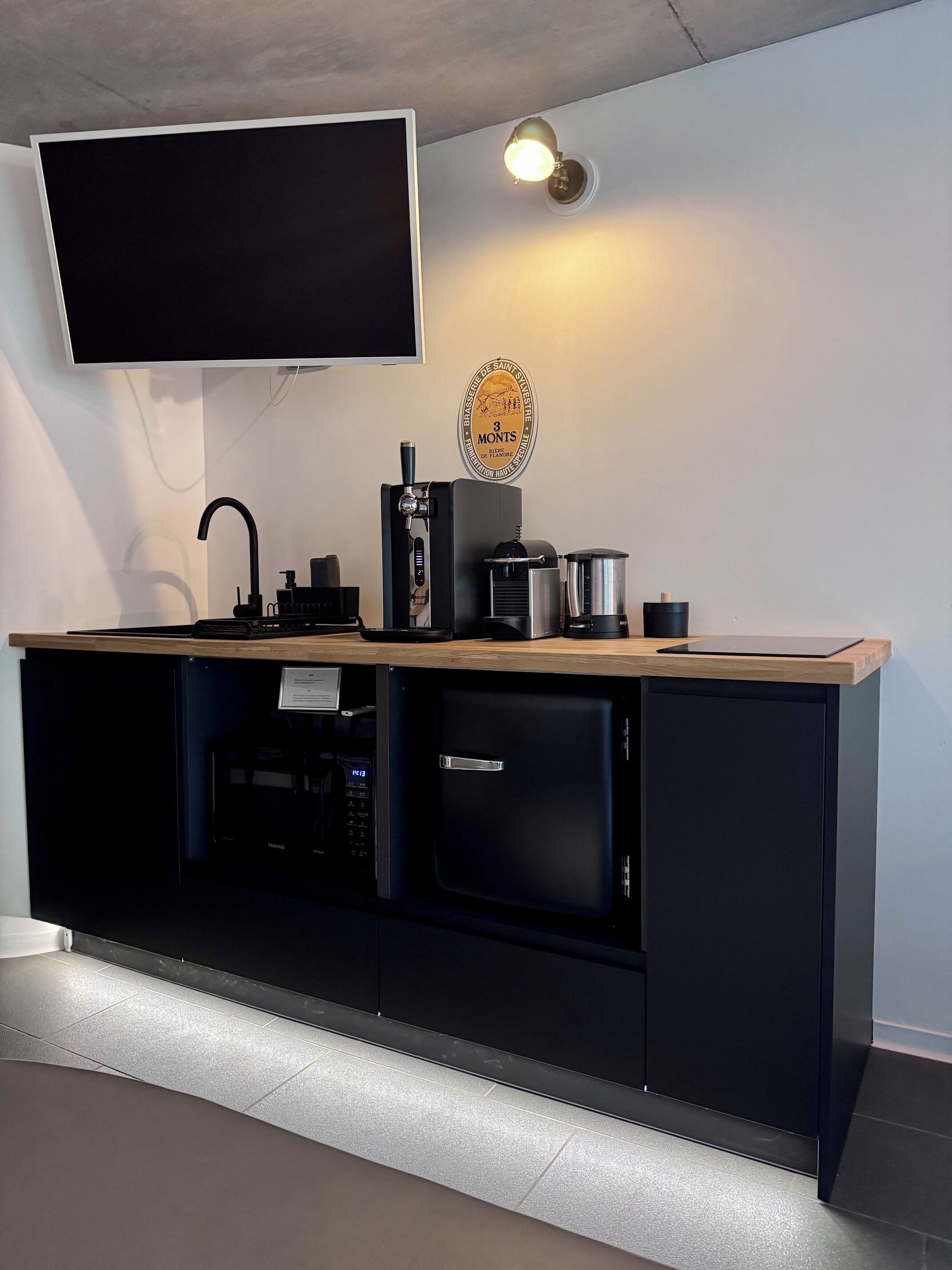 Una cocina moderna con televisor de pantalla plana, cafetera, hervidor y lavavajillas integrado.