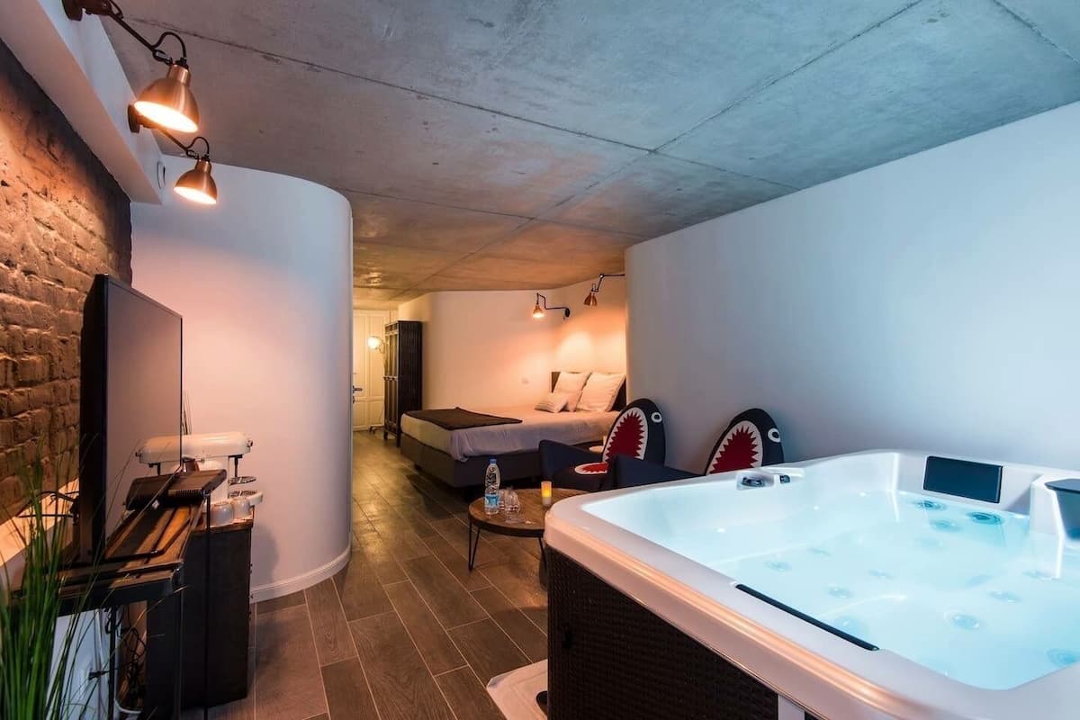 A modern hotel room with a large bathtub, a sofa, and a dining area with a table and chairs.