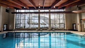 An indoor swimming pool with a view of snow-covered trees and buildings through large windows. - Pines 2169 (Keystone)
