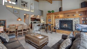 A spacious living room with a fireplace, a dining area with wooden furniture, and a kitchen in the background. - Pines 2169 (Keystone)