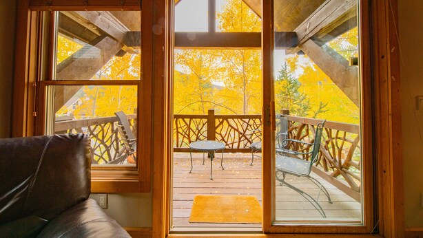 A wooden deck with a table and chairs, a wooden railing, and a view of autumn trees. - Cabin in the Pines 4 (Keystone)