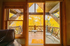 A wooden deck with a table and chairs, a wooden railing, and a view of autumn trees. - Cabin in the Pines 4 (Keystone)