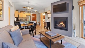 A modern living room with a fireplace, a dining area, and a kitchen in the background. - Silver Mill 8164 (Keystone)