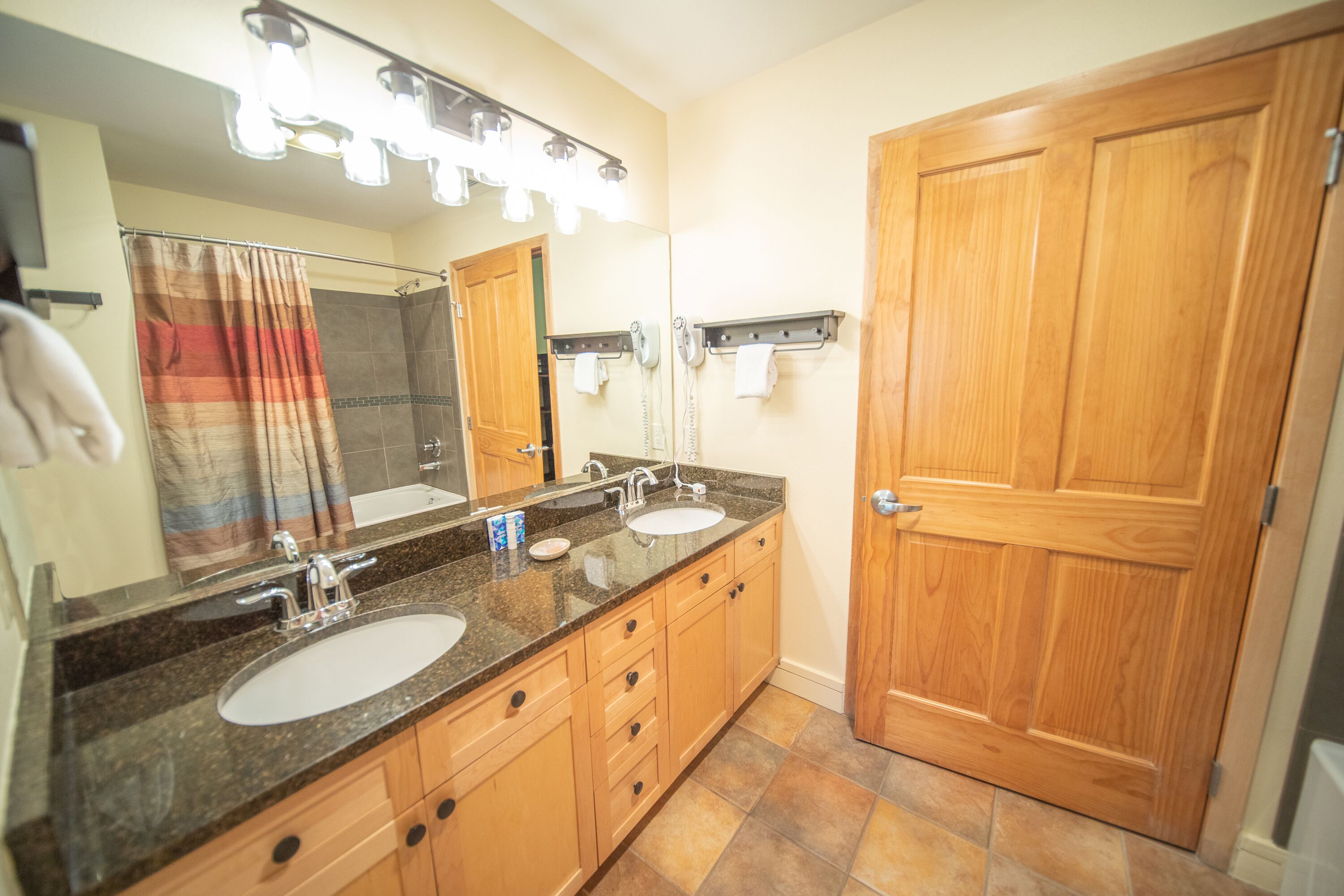 Une salle de bain avec deux lavabos, un miroir avec éclairage intégré, une douche et une porte en bois.