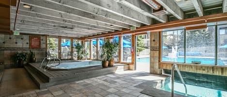 An indoor swimming pool with a wooden ceiling, tiled floor, and potted plants.