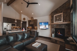 Ein modernes Wohnzimmer mit einer Ledersofa, einem Kamin, einem Fernseher und einer Küche im Hintergrund.