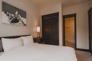 Ein Schlafzimmer mit einem großen Bett, einem Nachttisch mit Lampe, einem dunklen Holzschrank und einem Bild an der Wand.